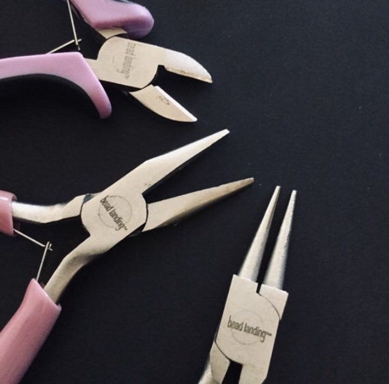 K&ouml;nnte beinhalten: Drei Paar Schmuckzangen mit rosa Griffen. Die Zangen sind mit "bead landing" beschriftet.