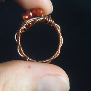 May include: A copper wire ring with three orange carnelian stones wrapped around the band.