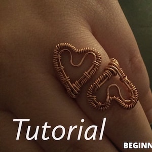 Puede incluir: Un anillo de alambre de cobre con dos formas de corazón entrelazadas. El anillo está en un dedo y la palabra "Tutorial" está escrita en texto blanco debajo del anillo. El texto "PRINCIPIANTE" está en la esquina inferior derecha.