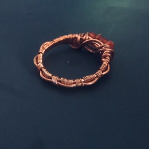 May include: A copper wire ring with three small orange stones set in the wire. The ring is on a dark blue background.