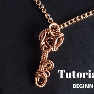 Puede incluir: Un collar con un colgante de llave de alambre de cobre y una cadena dorada. El colgante está hecho de alambre envuelto alrededor de sí mismo para crear una forma de llave. El collar es un tutorial para principiantes.