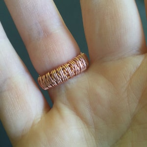 Peut inclure: Gros plan d'une bague en fil de cuivre sur le doigt d'une personne. La bague est compos&eacute;e de plusieurs brins de fil entrelac&eacute;s pour cr&eacute;er un design textur&eacute; et tress&eacute;.