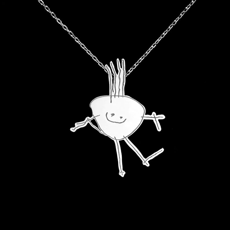 May include: A silver necklace with a pendant shaped like a child's drawing of a stick figure with a smiling face.