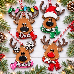 Pu&ograve; includere: Quattro decorazioni a forma di renna in legno con cordino rosso e bianco. Una ha una sciarpa rossa con la scritta Dad, una verde con Emmitt, una rosa con Isabell e una rossa con Mom. Ognuna presenta dettagli come luci natalizie, un cappello da Babbo Natale o fiocchi di neve bianchi.