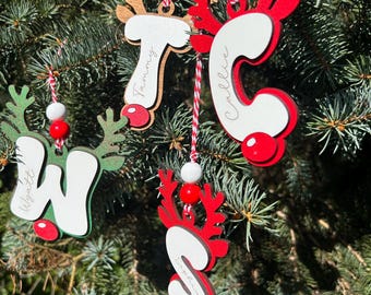 May include: Four personalized wooden letter ornaments shaped like reindeer with antlers. Each letter features a white front, a red or green base, and a red nose. The names Wyatt, Tammy, Callie, and Sophia are printed on the letters, which hang from red and white striped strings with white and red beads.
