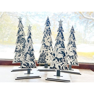 May include: Five black and white wooden Christmas trees with a decorative floral pattern. The trees are standing on a white surface.