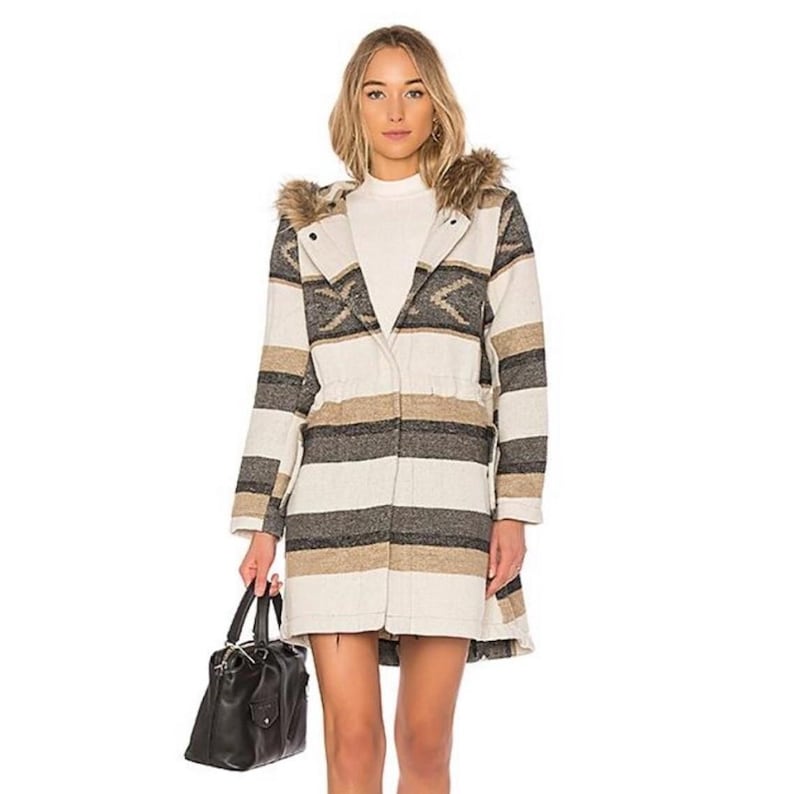 May include: A long coat with a hood and a fur trim. The coat features a striped pattern in cream, gray, and tan. It has a drawstring waist and is worn with a black handbag.
