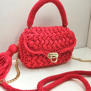 May include: A red crocheted handbag with a gold chain strap and a tassel. The bag has a flap closure with a gold clasp.