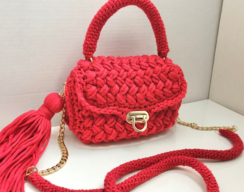 May include: A red crocheted handbag with a gold chain strap and a tassel. The bag has a flap closure with a gold clasp.
