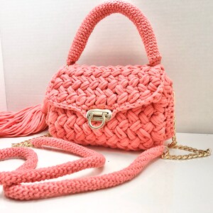 May include: A coral pink crocheted handbag with a gold chain strap and a tassel. The bag has a flap closure with a gold clasp.
