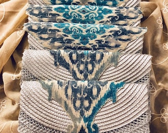 May include: A stack of silver and blue fabric clutches with an ikat pattern. The clutches are lined up in a row and have a beaded design.