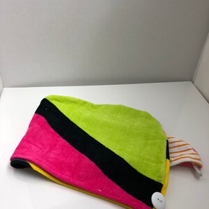 May include: A colorful hair towel with a black, pink, yellow, and green striped pattern. The towel has a white button and a striped fabric loop.