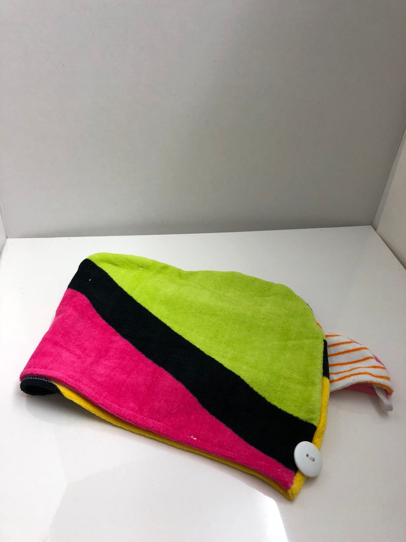 May include: A colorful hair towel with a black, pink, yellow, and green striped pattern. The towel has a white button and a striped fabric loop.