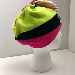 May include: A colorful striped towel turban in pink, green, black, white, and orange. The turban is made of soft, absorbent material and is designed to help keep hair dry after showering.