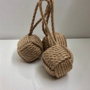 May include: Two brown rope doorstops with a knotted design. The rope doorstops are tied together with a loop.