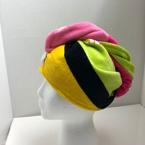 May include: A colorful striped hair towel with a button closure. The towel is pink, yellow, green, and black.