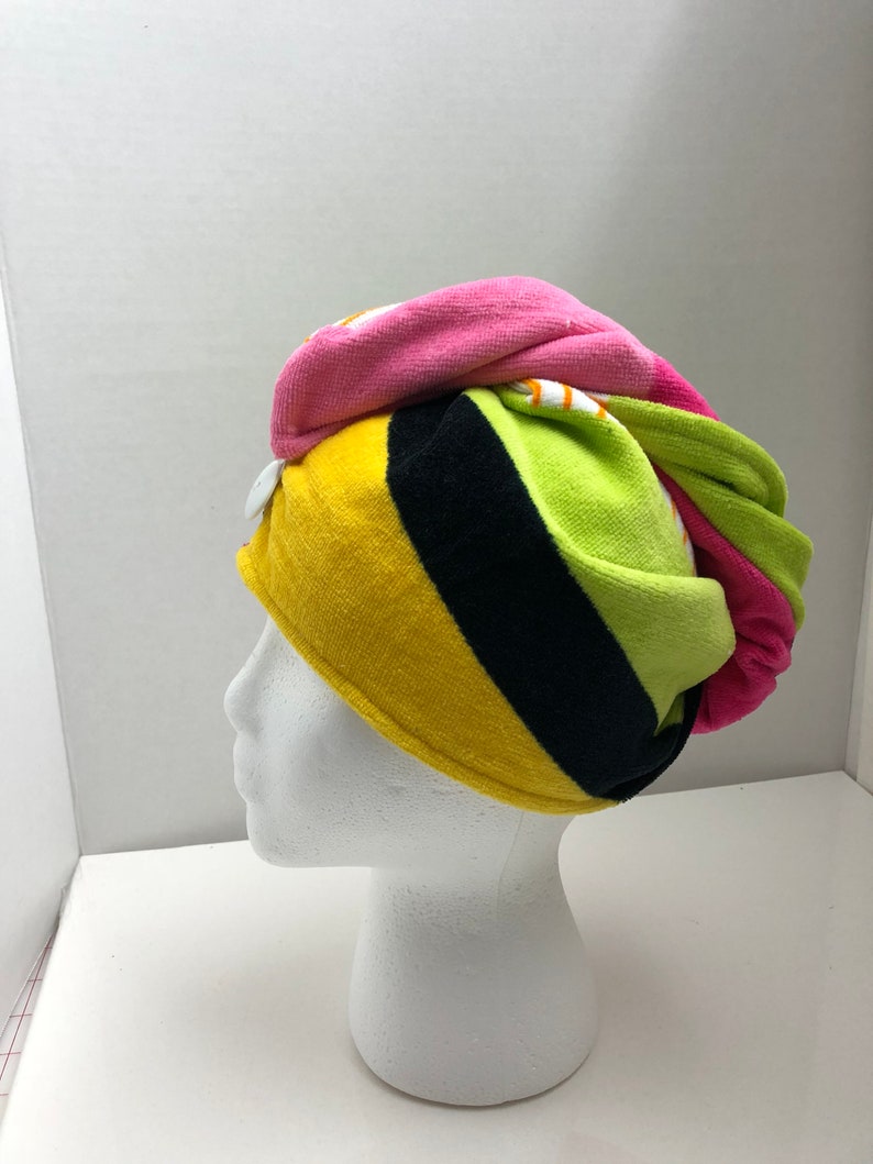 May include: A colorful striped hair towel with a button closure. The towel is pink, yellow, green, and black.