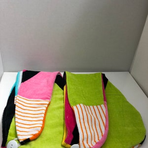 May include: Two colorful hair towels with a button closure. One towel is green, pink, black, and white. The other towel is green, yellow, pink, and black.
