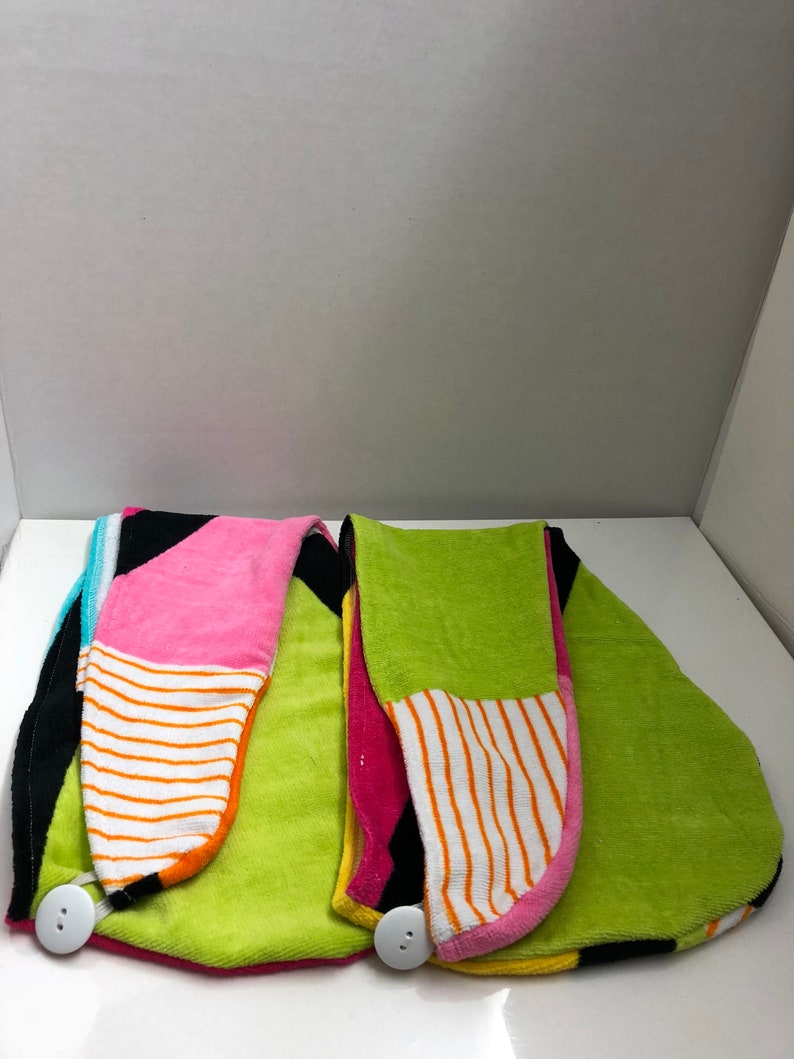 May include: Two colorful hair towels with a button closure. One towel is green, pink, black, and white. The other towel is green, yellow, pink, and black.