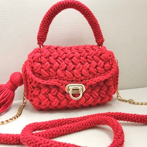 May include: A red crocheted handbag with a gold chain strap and a tassel. The bag has a gold clasp and a top handle.