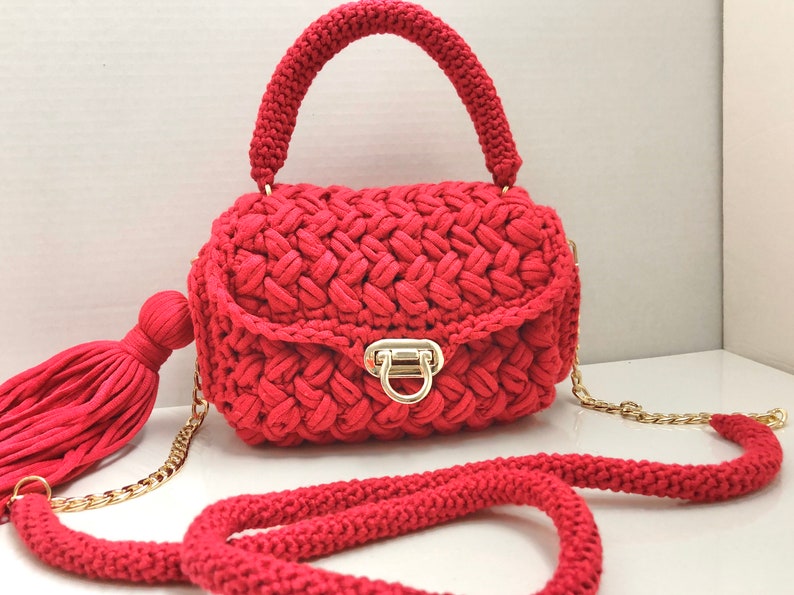 May include: A red crocheted handbag with a gold chain strap and a tassel. The bag has a gold clasp and a top handle.