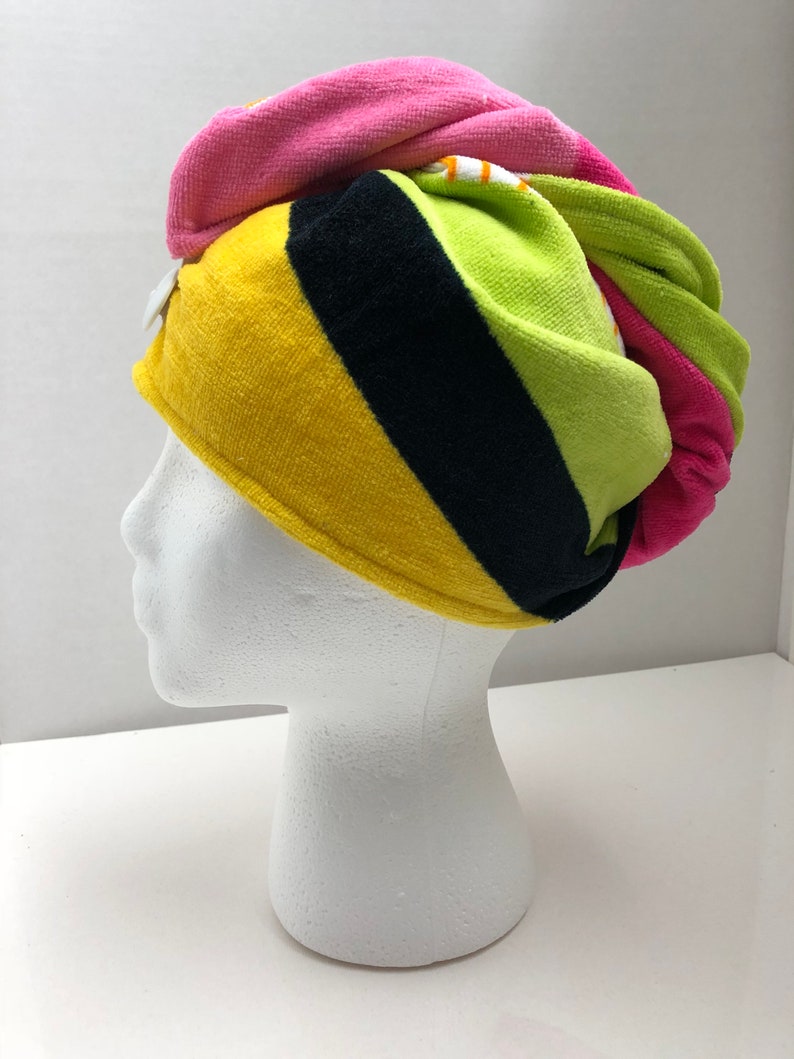 May include: A colorful striped hair towel in pink, yellow, green, and black. The towel is wrapped around a white mannequin head.