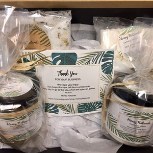 May include: A gift basket filled with bath and body products from Honey Naturals. The basket includes a bar of soap, a jar of body butter, a jar of sugar scrub, and a jar of lip balm. The basket is decorated with a thank you card and a tropical leaf design.