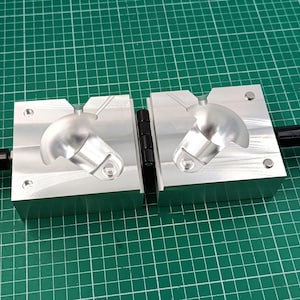 Può includere: Stampo in alluminio a due pezzi con manico nero. Lo stampo è aperto e ha due cavità a forma di semisfera.