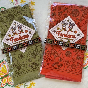 two colors of WDW golden anniversary shown in their packaging with true vintage 1970s flowered trim tied around them on true vintage 1970s fabric sheet with butterflies