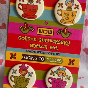 May include: Set of four colorful button pins featuring a vintage illustration of a doll sitting in a teacup. The buttons are on a card with the text "Golden Anniversary Button Set" and "Made with Love by Going to Guides".