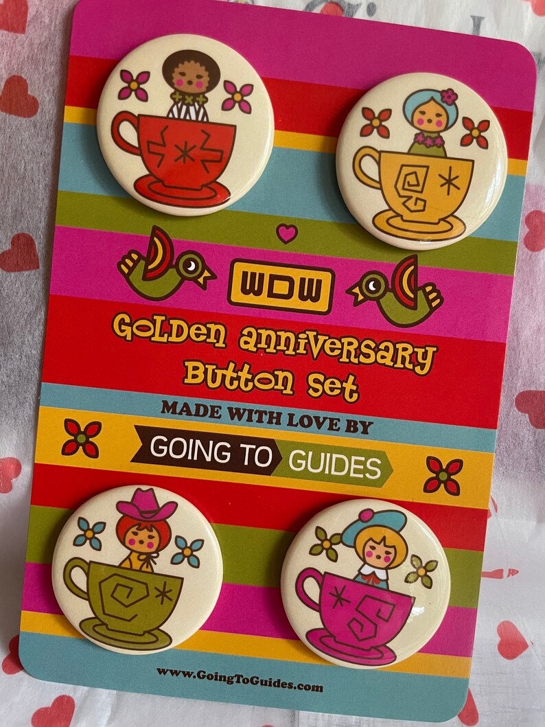 May include: Set of four colorful button pins featuring a vintage illustration of a doll sitting in a teacup. The buttons are on a card with the text "Golden Anniversary Button Set" and "Made with Love by Going to Guides".