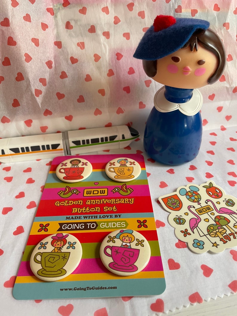 May include: A set of four colorful button pins featuring a cartoon character in a teacup. The buttons are packaged on a card with the text "WOW Golden Anniversary Button Set Made with Love by Going to Guides www.GoingToGuides.com".