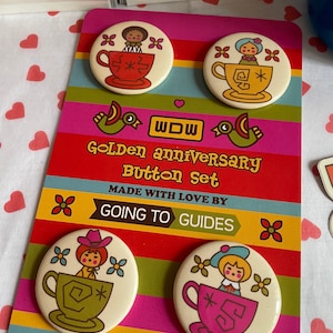 May include: Set of four 2.25 inch diameter button pins featuring vintage-style illustrations of dolls in teacups. The buttons are on a card with the text "Golden Anniversary Button Set" and "Made with love by Going to Guides".