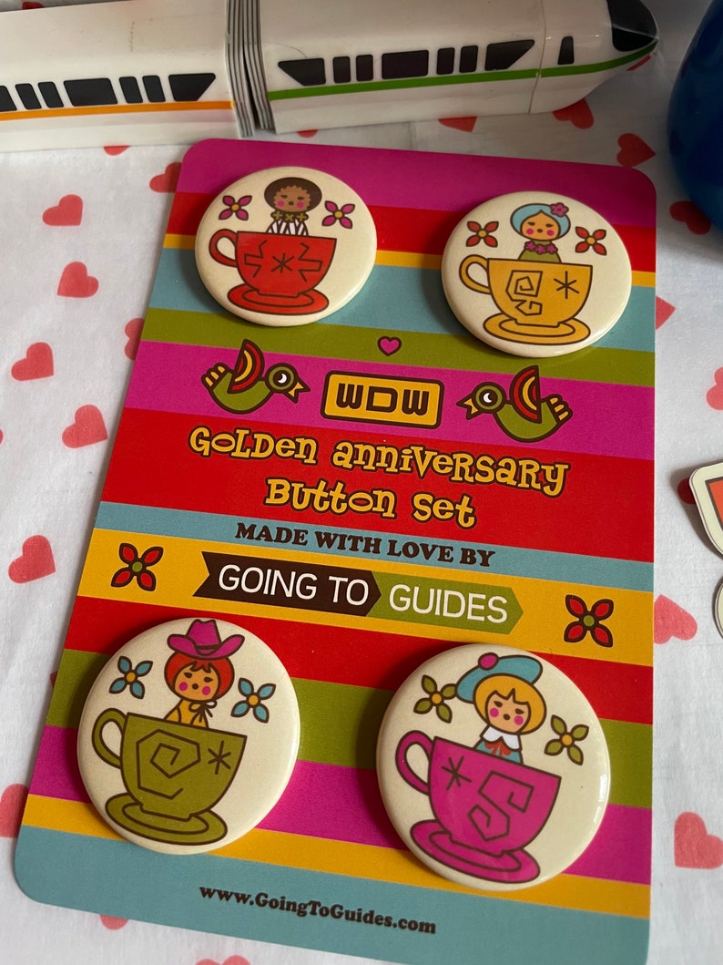 May include: Set of four 2.25 inch diameter button pins featuring vintage-style illustrations of dolls in teacups. The buttons are on a card with the text "Golden Anniversary Button Set" and "Made with love by Going to Guides".