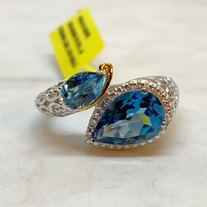 Könnte beinhalten: Ein silberner Ring mit einem birnenförmigen blauen Topas-Edelstein, der in einer goldenen Fassung sitzt. Der Ring hat ein filigranes Design und einen kleineren blauen Topas-Edelstein an der Seite.