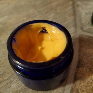 May include: A blue jar with a yellow cream inside. The cream is thick and has a smooth texture.