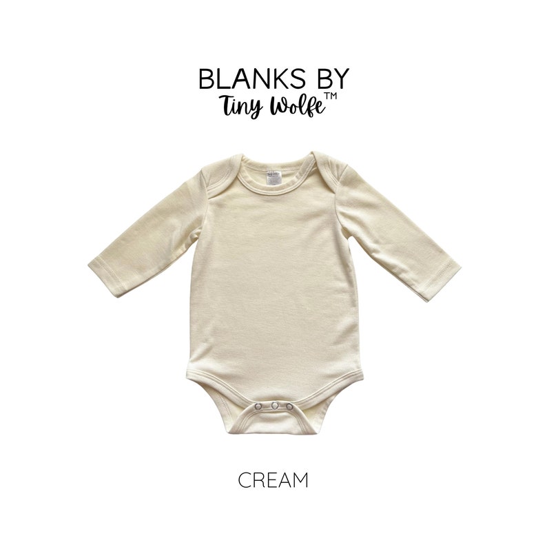 K&ouml;nnte beinhalten: Ein cremefarbener lang&auml;rmeliger Baby-Body mit Rundhalsausschnitt und Druckkn&ouml;pfen. Der Body ist aus weichem, bequemem Stoff gefertigt. Blanks by Tiny Wolfe ist oben auf dem Body gedruckt. Das Wort "CREAM" ist unter dem Body gedruckt.