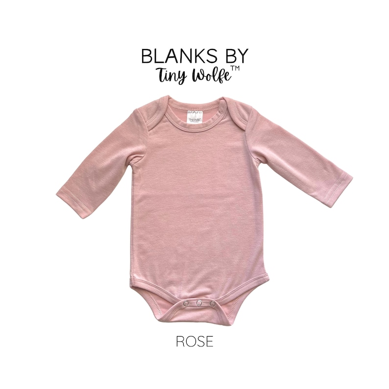 K&ouml;nnte beinhalten: Ein lang&auml;rmliger Baby-Body in zartem Rosaton. Der Body hat einen Rundhalsausschnitt und Druckkn&ouml;pfe am unteren Ende. Der Text "Blanks by Tiny Wolfe" ist auf wei&szlig;em Hintergrund &uuml;ber dem Body gedruckt. Das Wort "ROSE" ist unter dem Body gedruckt.