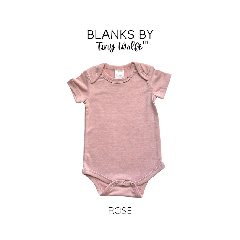 May include: A plain rose-colored baby onesie with short sleeves. The onesie has a snap closure at the bottom and is made of a soft, comfortable fabric. The text "Blanks by Tiny Wolfe" is printed above the onesie. The word "ROSE" is printed below the onesie.
