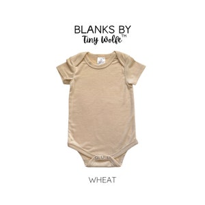 May include: A plain, wheat-colored baby onesie with short sleeves and snap closures. The onesie is made by Blanks by Tiny Wolfe.
