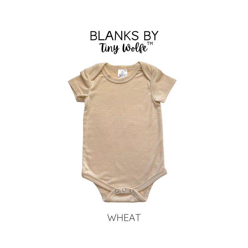 May include: A plain, wheat-colored baby onesie with short sleeves and snap closures. The onesie is made by Blanks by Tiny Wolfe.
