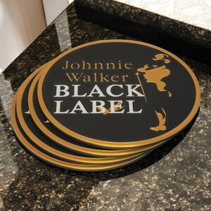 K&ouml;nnte beinhalten: Ein Stapel schwarzer, runder Untersetzer mit goldenem Rand. Die Untersetzer zeigen die Worte "Johnnie Walker BLACK LABEL" in Gold und Wei&szlig; sowie eine goldene Silhouette eines Mannes.