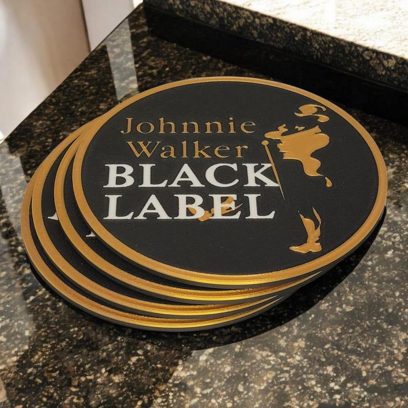 K&ouml;nnte beinhalten: Ein Stapel schwarzer, runder Untersetzer mit goldenem Rand. Die Untersetzer zeigen die Worte "Johnnie Walker BLACK LABEL" in Gold und Wei&szlig; sowie eine goldene Silhouette eines Mannes.