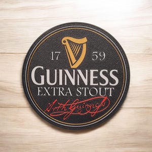 K&ouml;nnte beinhalten: Ein runder, schwarzer Guinness Extra Stout Untersetzer mit einem goldenen Harfenlogo, den Zahlen 17 und 59 und der Unterschrift "Arth Guinness" in roter Schrift. Der Untersetzer hat eine strukturierte Oberfl&auml;che und einen goldenen Rand.