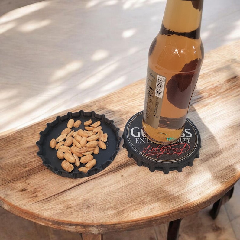 K&ouml;nnte beinhalten: Ein schwarzer Untersetzer in Form eines Flaschenverschlusses mit dem Text "Guinness Extra Stout" tr&auml;gt eine Bierflasche. Ein zweiter schwarzer Teller in Form eines Flaschenverschlusses enth&auml;lt Erdn&uuml;sse. Die Artikel liegen auf einem Holztisch.