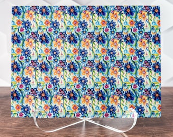 May include: A colorful floral print with blue, yellow, and orange flowers on a white background. The print is on a glass cutting board with a clear acrylic stand.