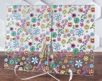 May include: A clear glass picture frame with a colorful floral pattern. The frame is on a clear acrylic stand.