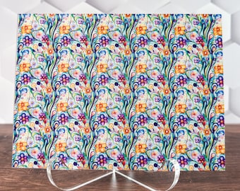 May include: A decorative glass cutting board with a colorful floral pattern. The pattern features blue, purple, yellow, and orange flowers and swirls on a white background.