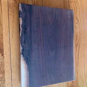 May include: A large, dark brown wooden cutting board with a natural edge. The board has a smooth surface and is made of solid wood.