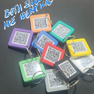 May include: A collection of colorful square keychains, each with a QR code and a metal ring. The keychains are in various colors, including purple, orange, green, blue, red, yellow, black, and white. The text "BOTH SIDES ARE IDENTICAL" is written in blue and white.